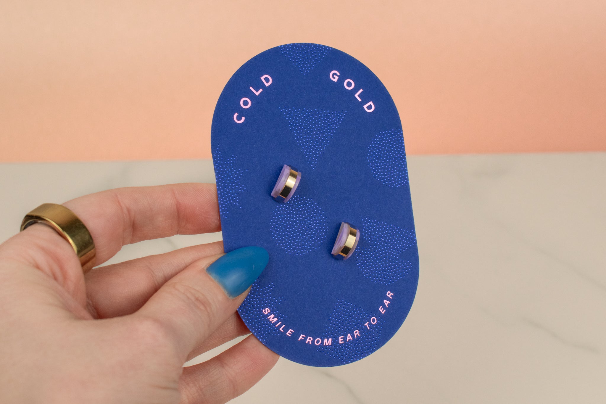 hand holding bright blue cold gold card displaying amethyst gold hoop earrings