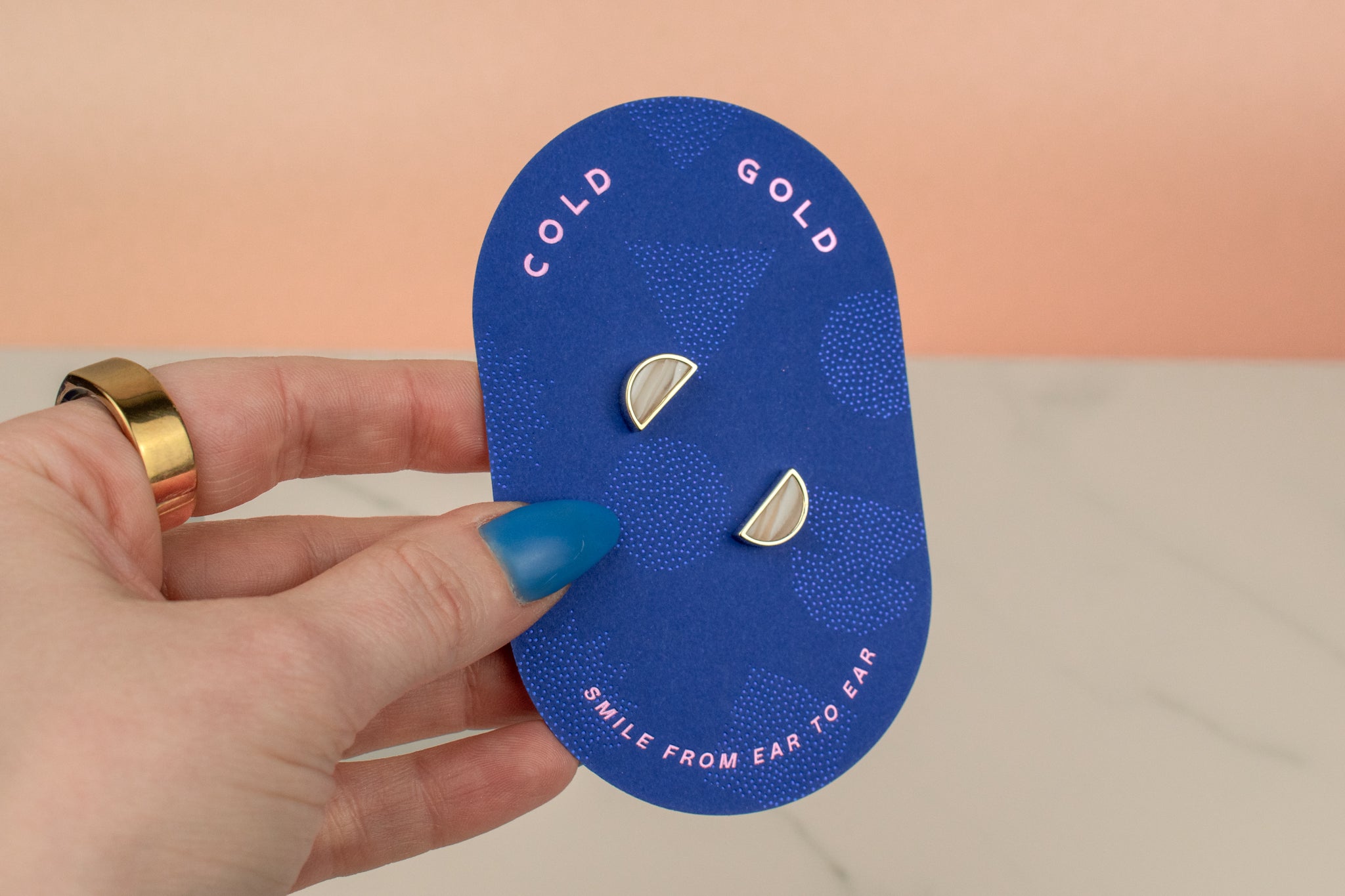 hand holding blue card displaying polymer clay hand marbled crystal quartz white geometric gold half moon stud earrings