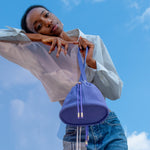 model leaning on piece of colored acrylic displaying purple nubuck bucket bag