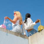 models sitting on ledge posing with metallic pink and pistachio leather slouchy bags