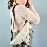 a woman wears a cowprint sling bag for bonnaroo essentials bag small leather sling bag crossbody cowhide leather purse cowprint gift for sister sling purse with inside pocket over her shoulder