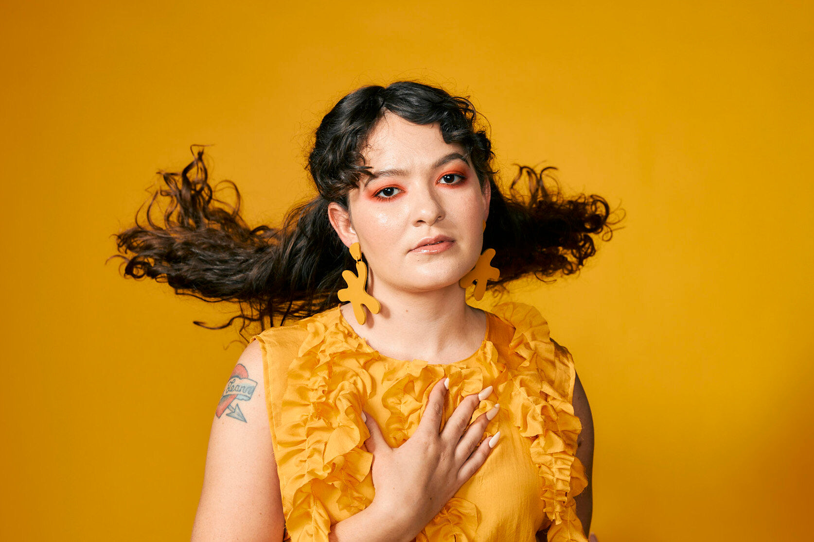 bold and modern yellow leather earrings in marigold on a woman with long curly dark hair.