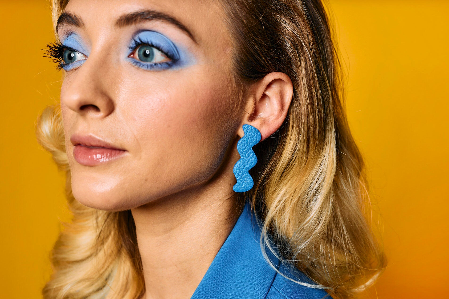 woman with blue makeup and blonde hair wearing Matisse blue cutout statement leather zig zag earrings.