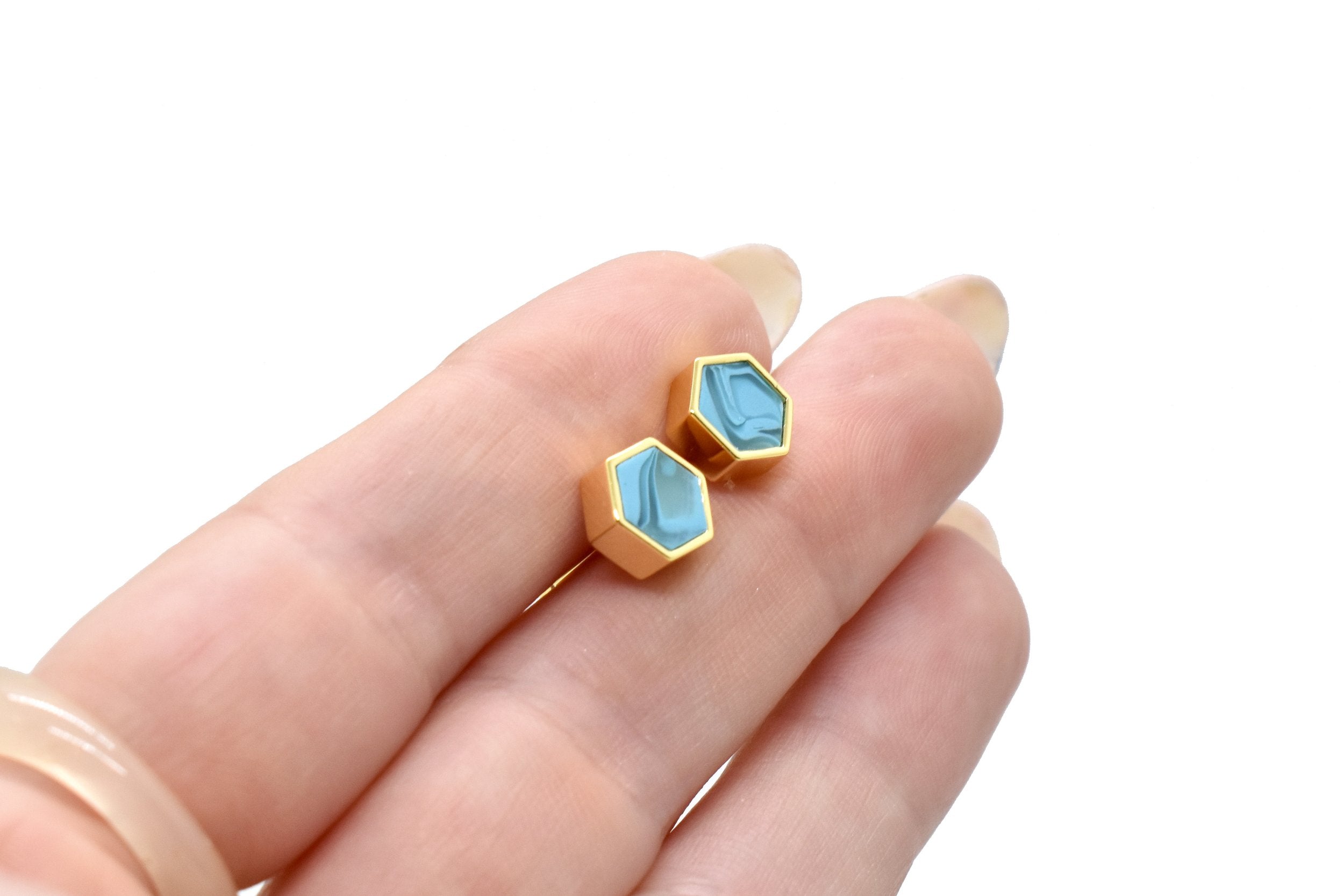 hand holding a pair of modern and minimal stud earrings in aqua crystal clay and gold