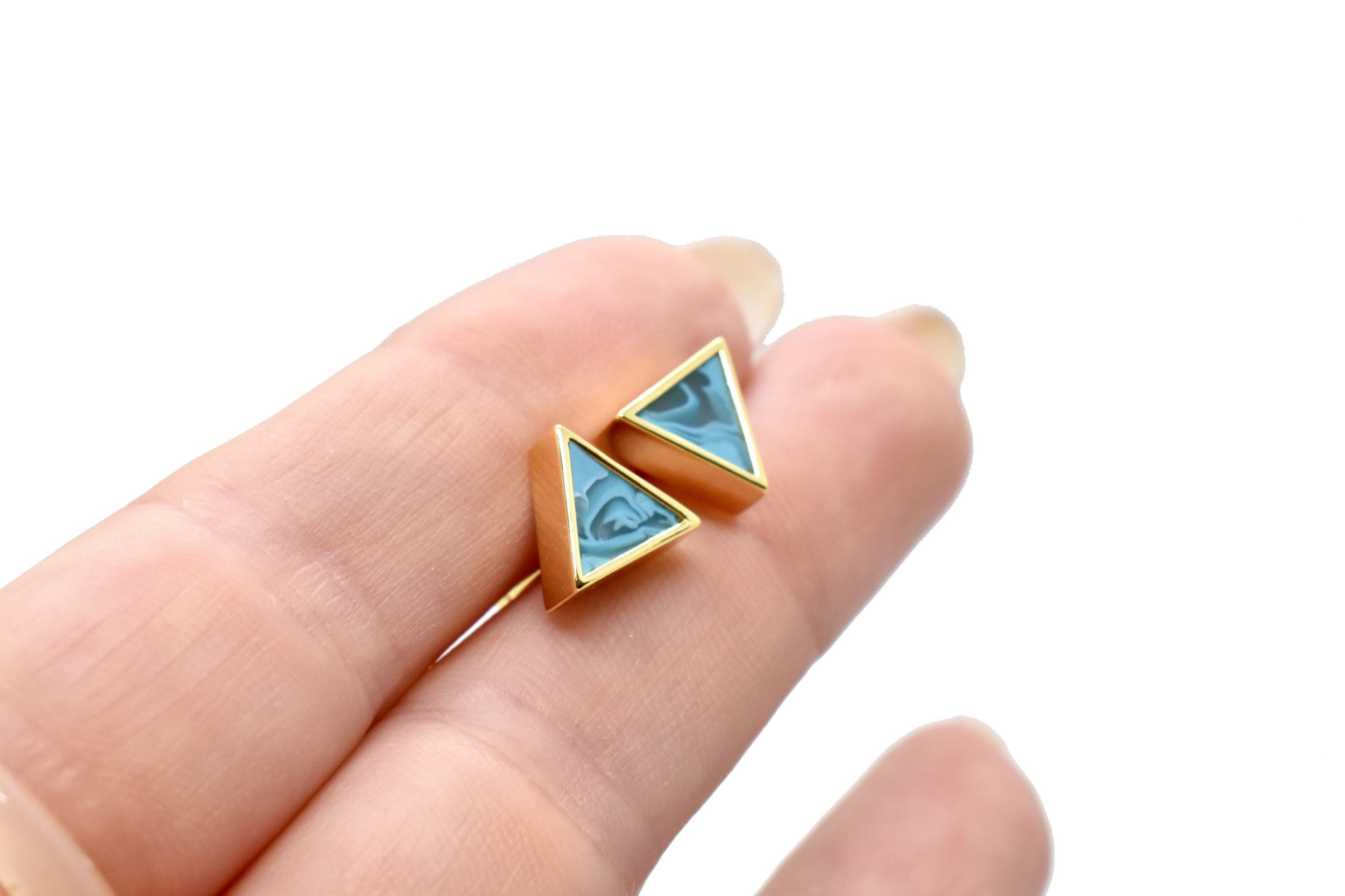 hands holding a pair of small geometric triangle earring stud set in gold and aquamarine
