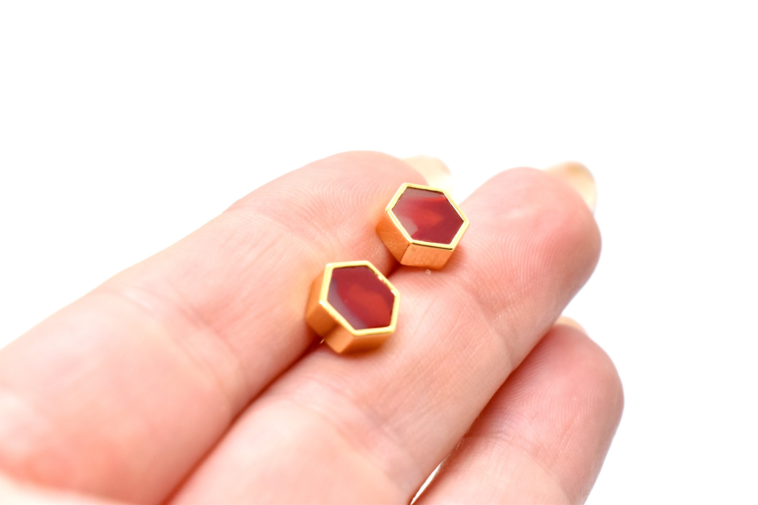 hand holding a pair of studs with 24k gold hexagons and ruby garnet gemstone modern studs against white background