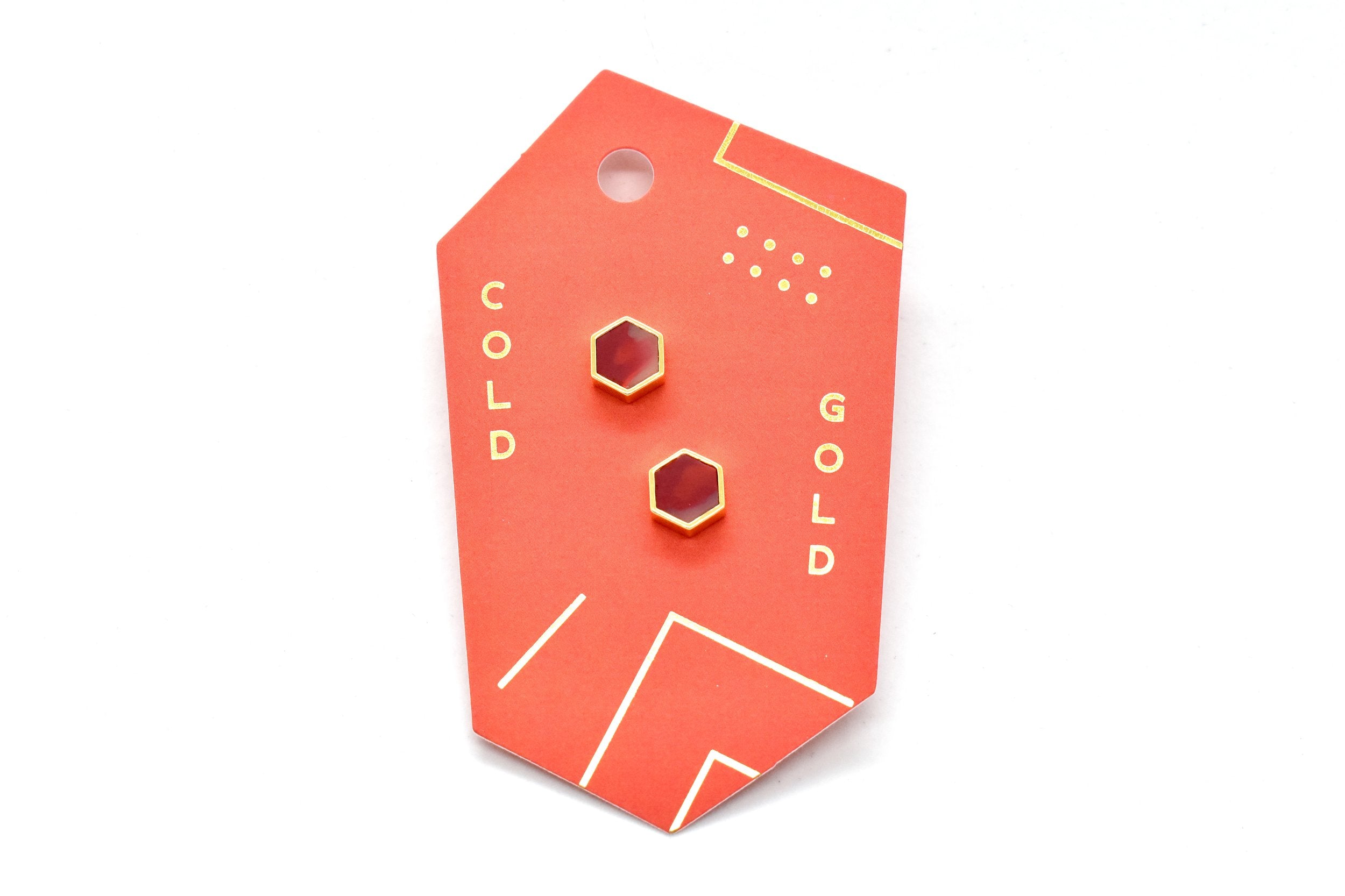 a red card showing a set of gold studs with ruby stone that is marbled polymer clay