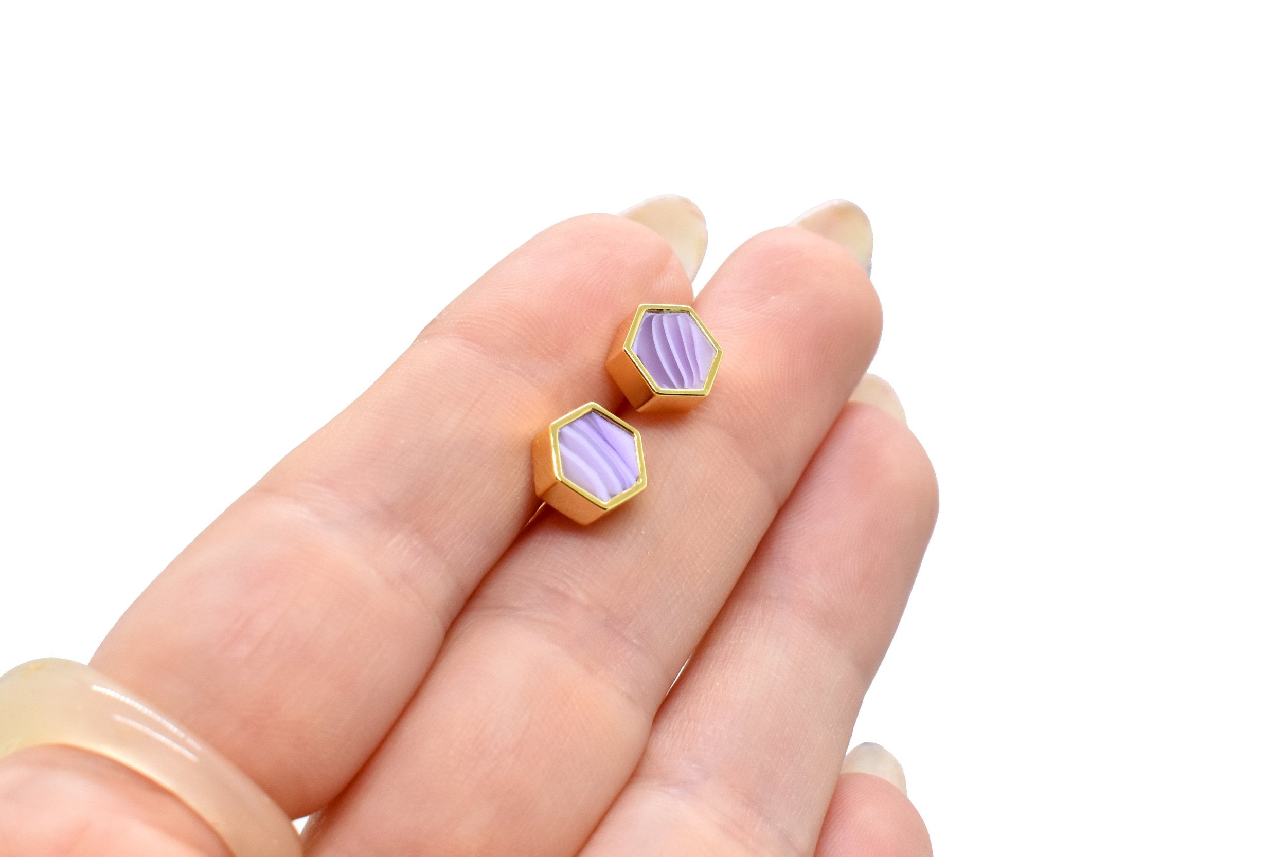 hands holding a pair of lilac hexagon gold stud earrings