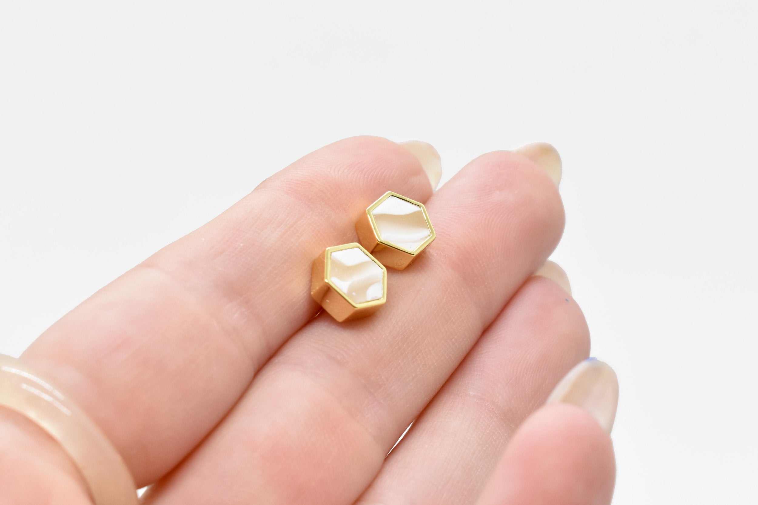 hand holding modern and minimal hexagon stud earrings in vanilla crystal quartz and gold