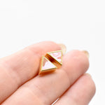 a hand holding a tiny pair of studs in pastel pink tiny triangle earrings with 24k gold plating.