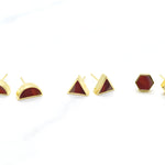 a set of three pairs of gold geometric stud earrings. One set of triangle studs, one set of gold hexagon earrings and one set of half moon stud earrings, all in ruby gemstone that's been marbled