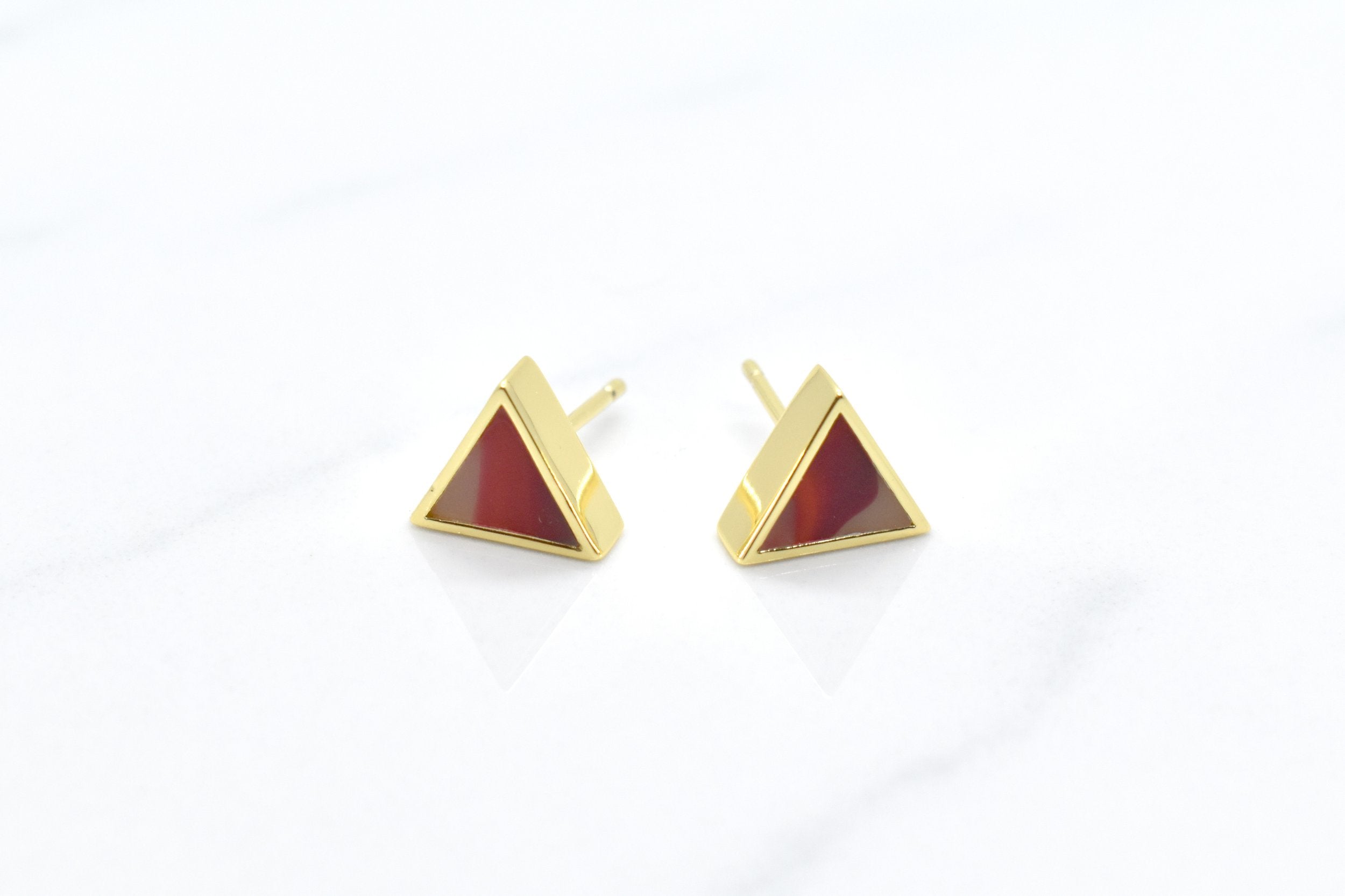 gold triangle stud earring set in ruby gemstone like clay against a white background