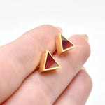 hands holding a pair of geometric triangle stud earrings in garnet red with gemstone texture clay, hand marbled to look like sapphire, a perfect gift for a July birthday