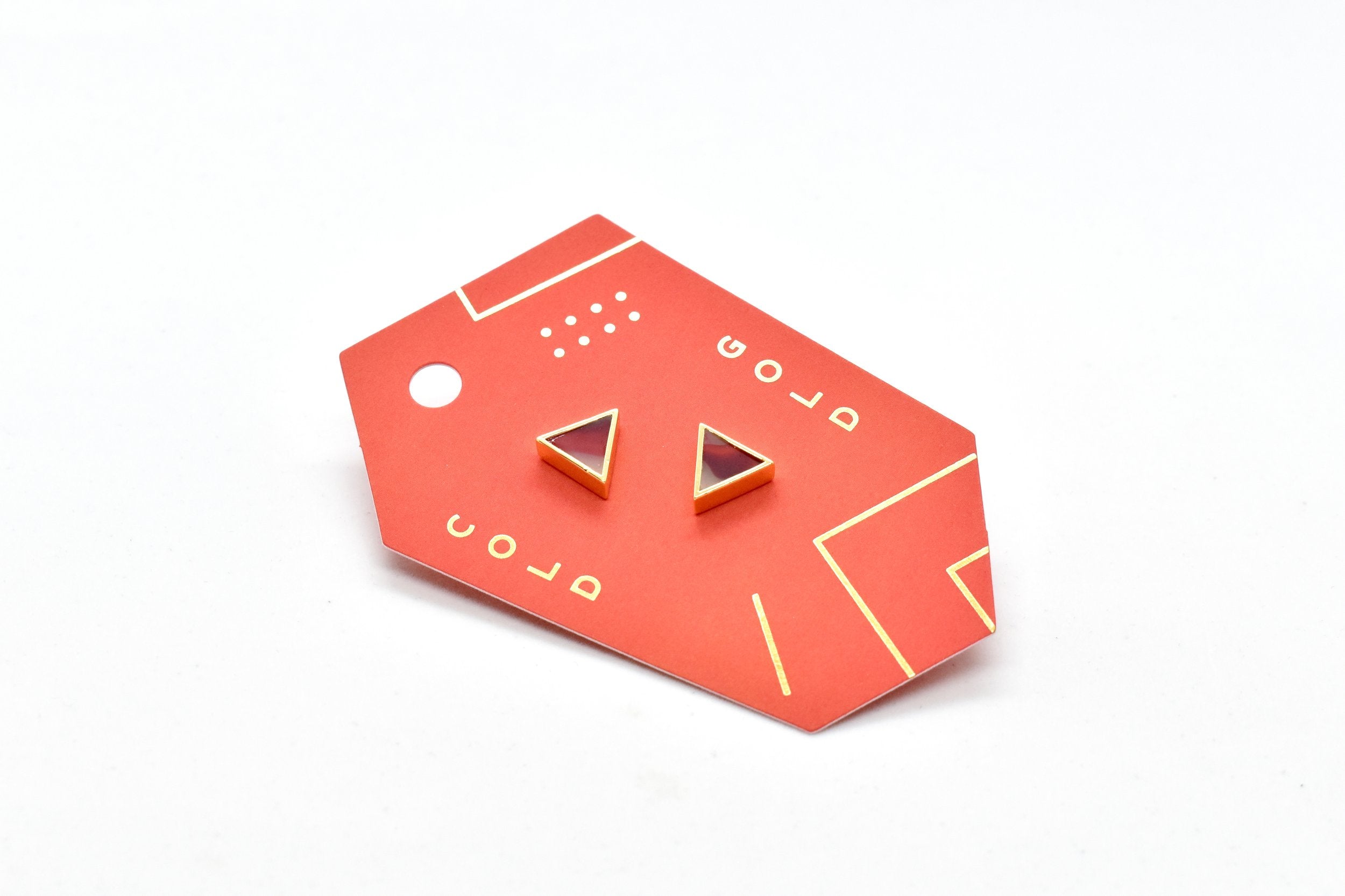 red geometric card with ruby studs in a 24k gold triangle shape, geometric jewelry made for sensitive ears shown with ruby pattern and watercolor texture