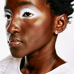 A woman with short hair and dramatic white makeup wears art-deco inspired stud earrings in semi-transparent pink clay and gold.