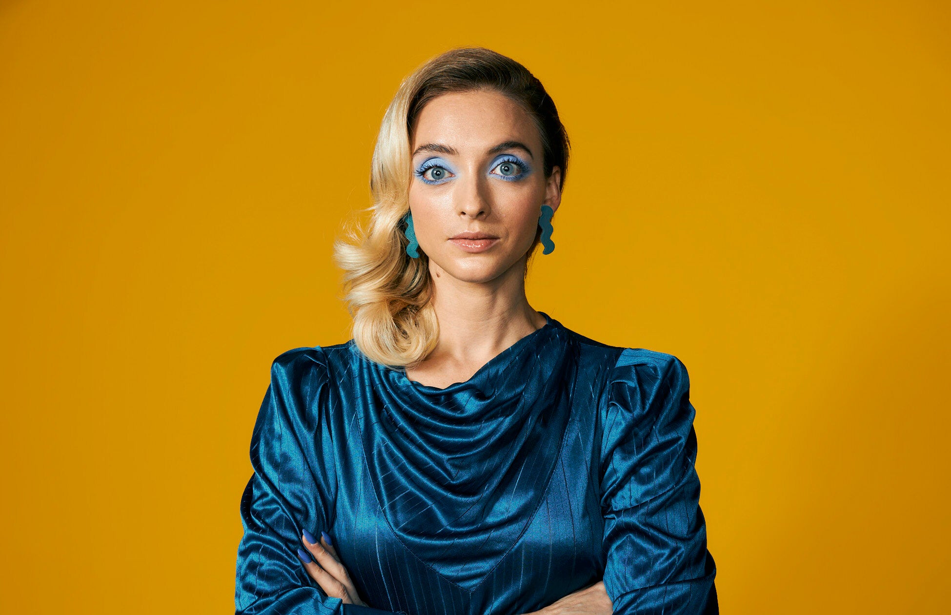 a blonde woman wearing a vintage draped turquoise dress with lightning bolt earrings in turquoise.