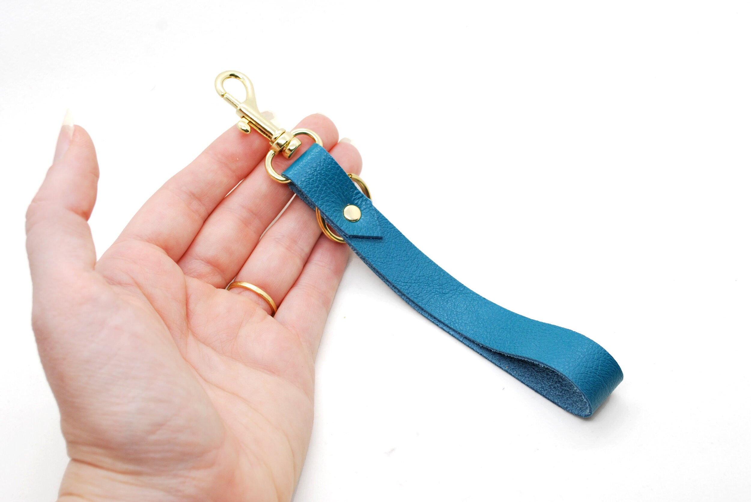 hand holding a turquoise leather keychain wristlet with gold clasp and key ring.