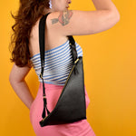 Person show from side wearing a leather wristlet pouch with an adjustable strap on her shoulder