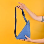 a pair of hands shown holding a matisse style sling bag purse in leather blue as a crossbody outdoor hiking bag