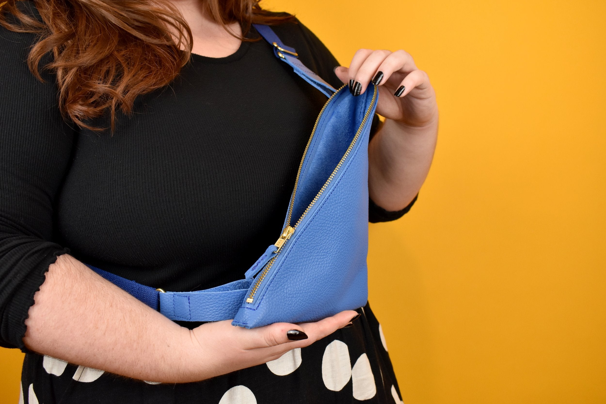 person shown opening a bright blue leather purse that lays across their chest