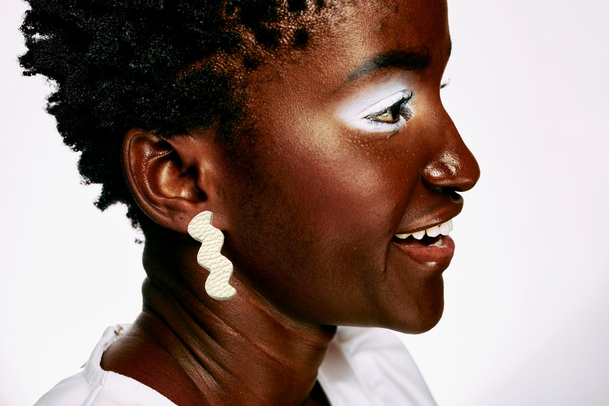 A young woman wears the light trace earrings in bone white real leather