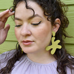 A woman wears large dangling star-shape earrings in chartreuseleather