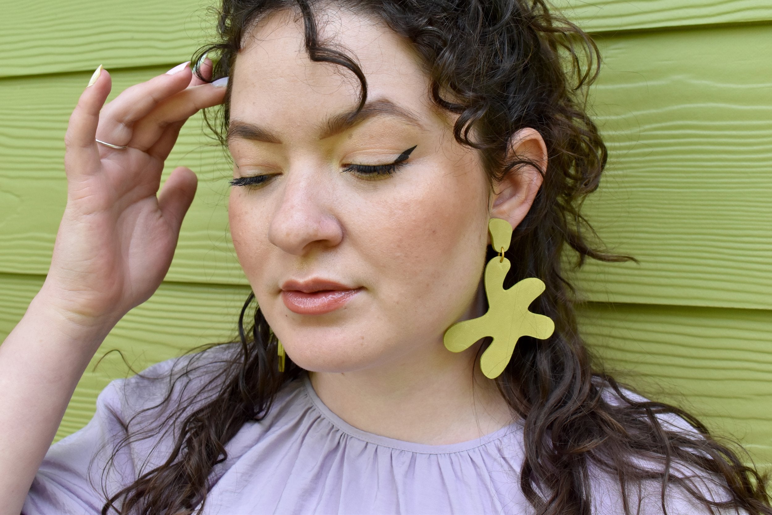 A woman wears large dangling star-shape earrings in chartreuseleather