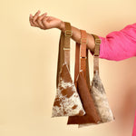 a set of three chestnut hair on hide leather sling bag cowgirl accessory leather cowhide neutral leather sling gift for daughter gift for hiker bachelorette party gifts draped over a womans arm