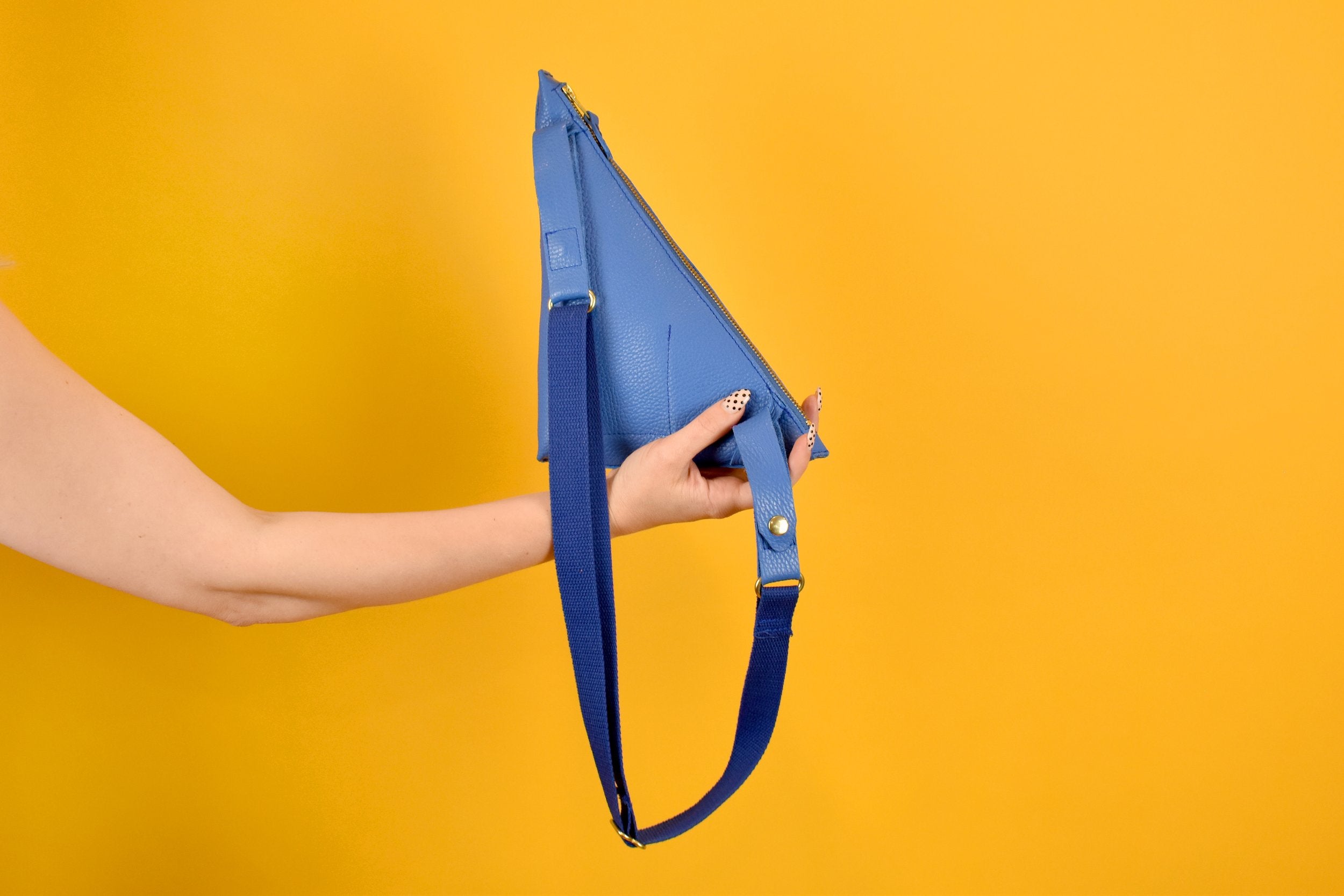 a hand holding a lightweight bag triangle shape accessory with a long strap perfect for music festivals like coachella bag