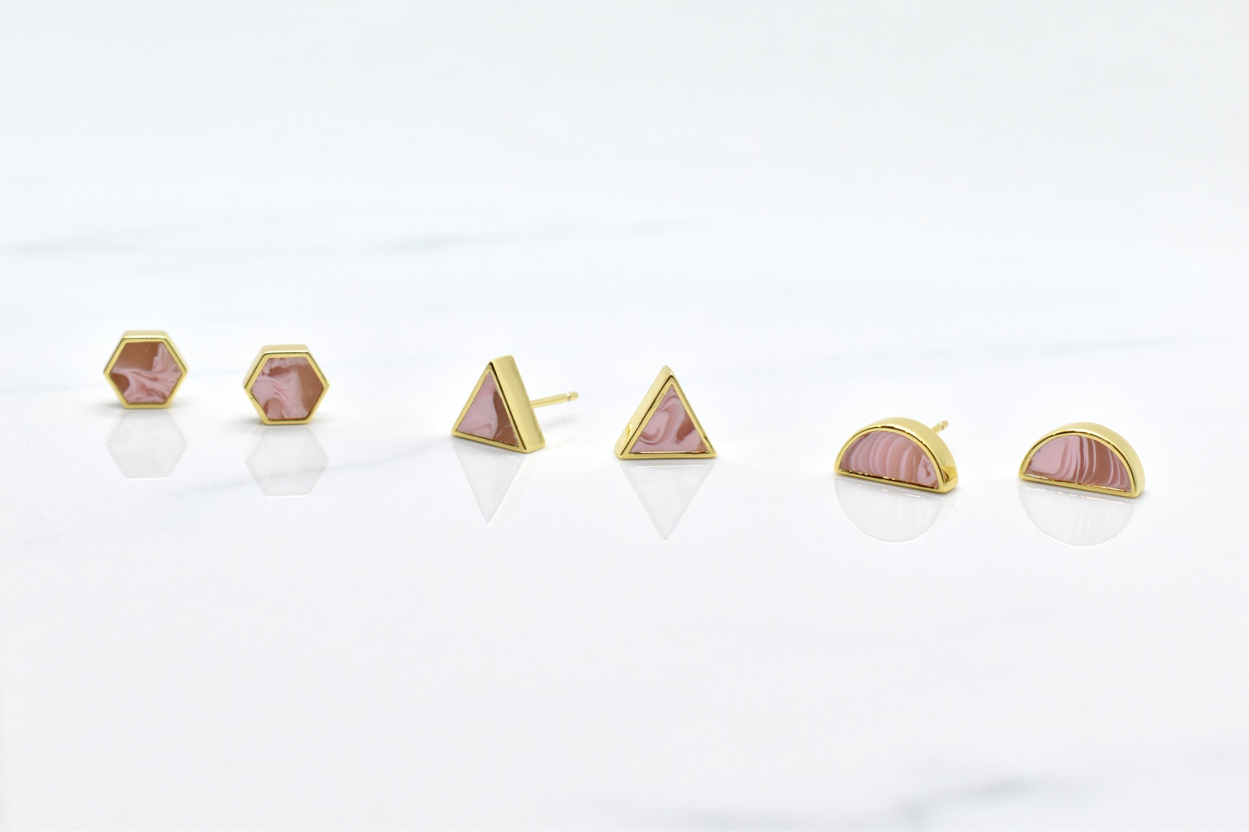 set of three geometric earrings in candy pink swirls in hexagon, triangle, and half moon shapes with gold accents and studs.