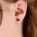 a close up photo on a model of the tiny ruby earrings in a triangle shape with 24k gold plating