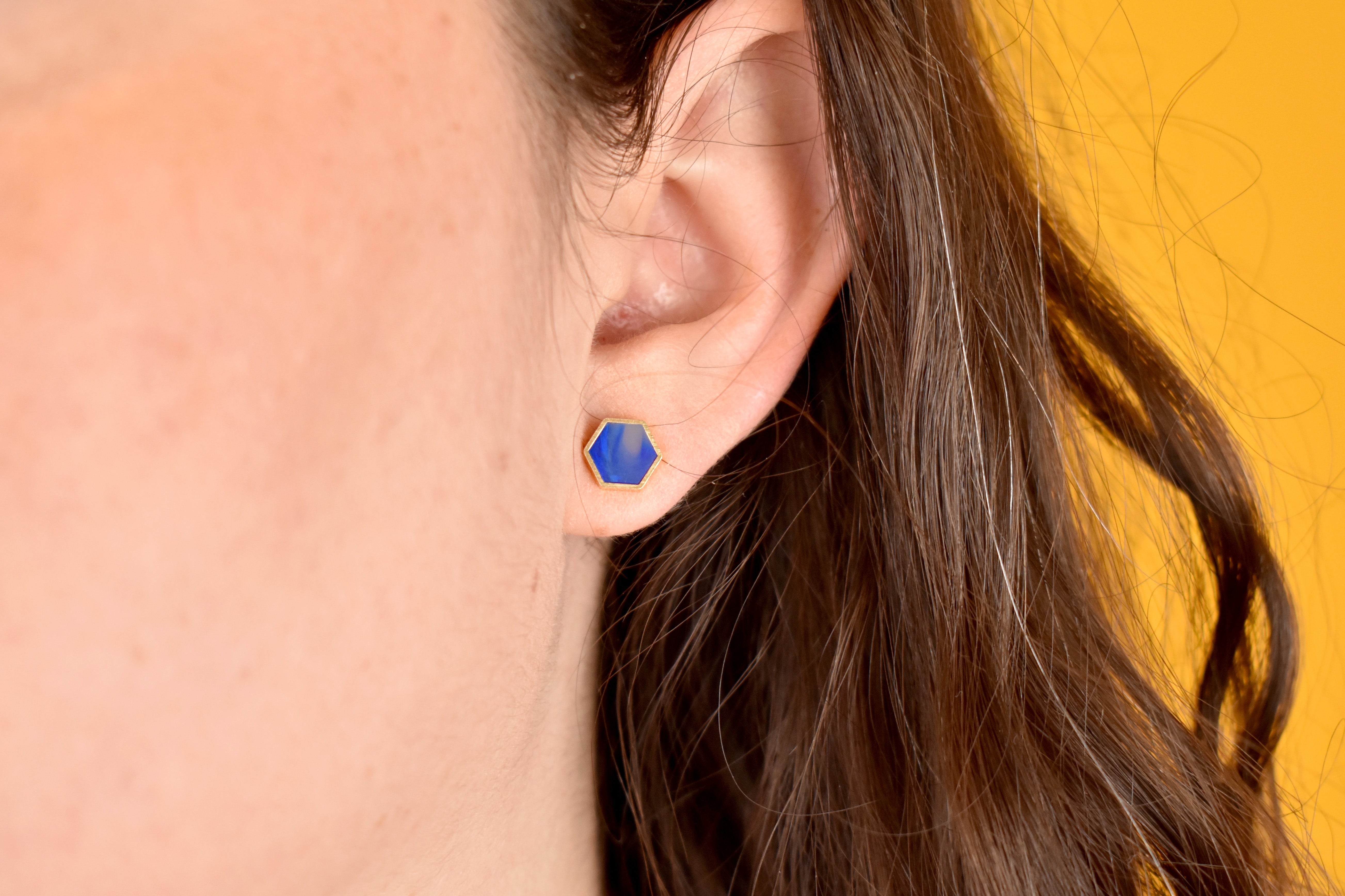model wears a geometric stud earring in triangle stud shape with sapphire marbled clay