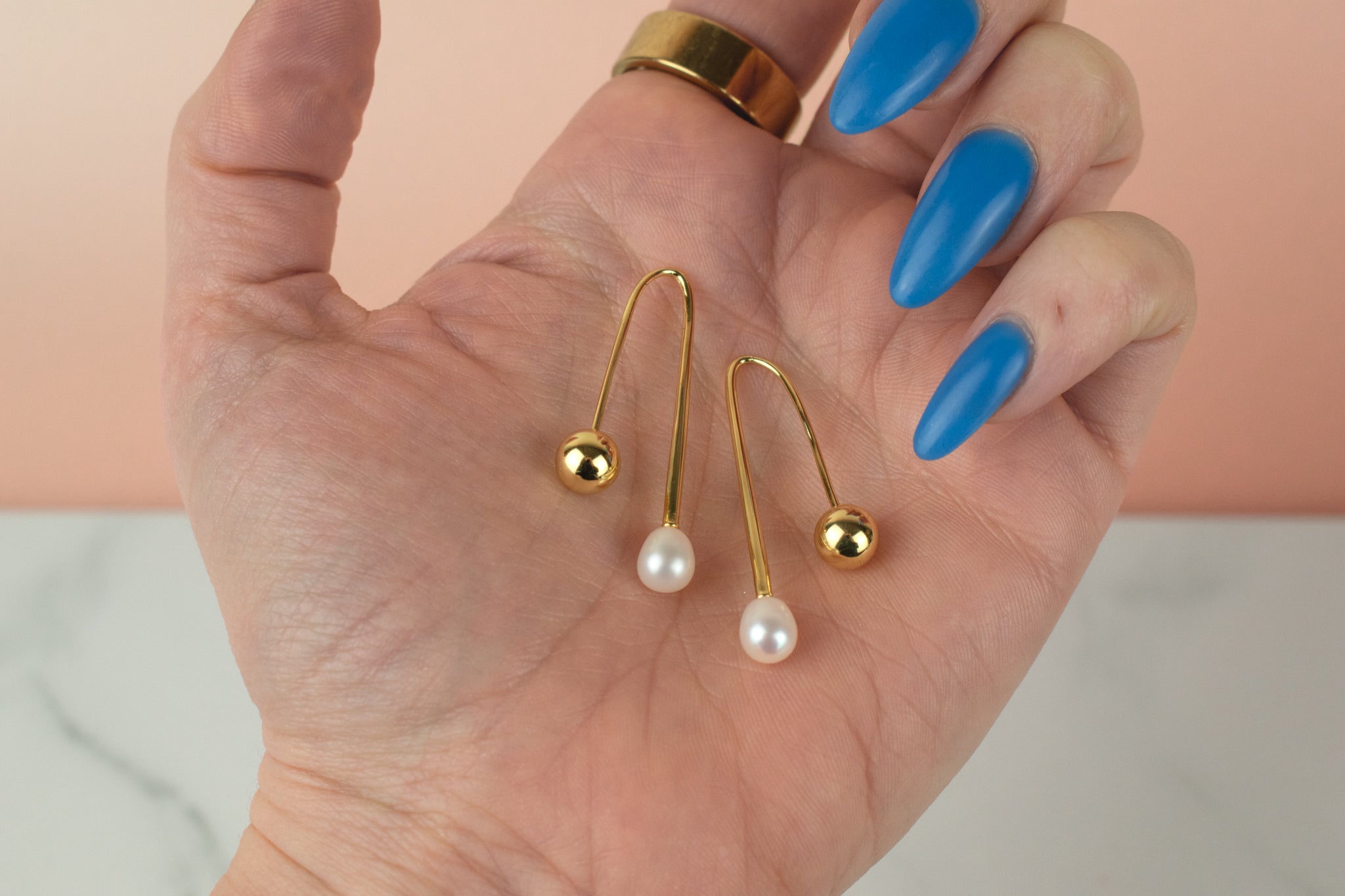 a hand holds a pair of gold freshwater baroque pearl drop earrings