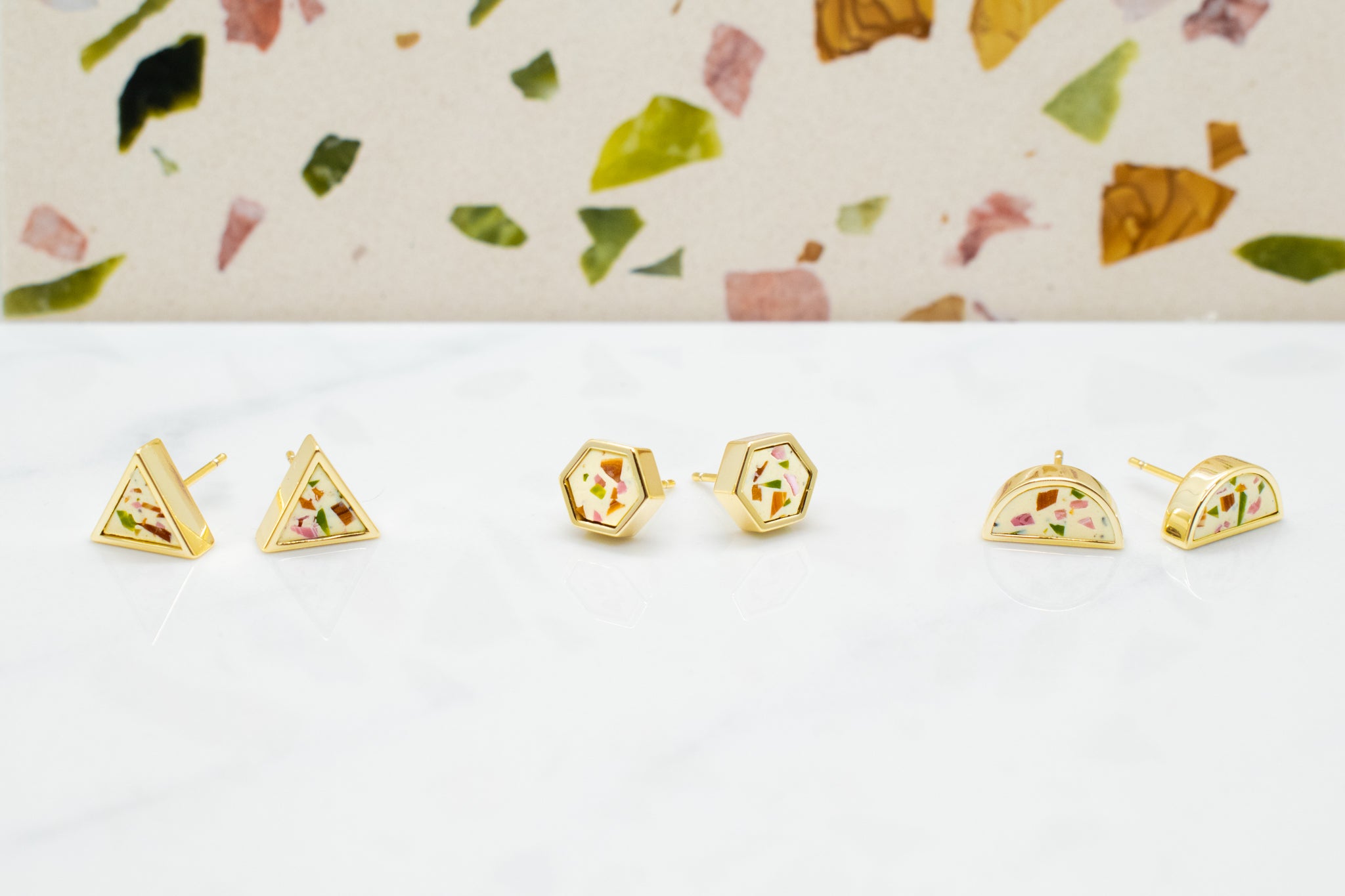 three available shapes of white terrazzo gold geometric studs: triangle, hexagon, and half moons