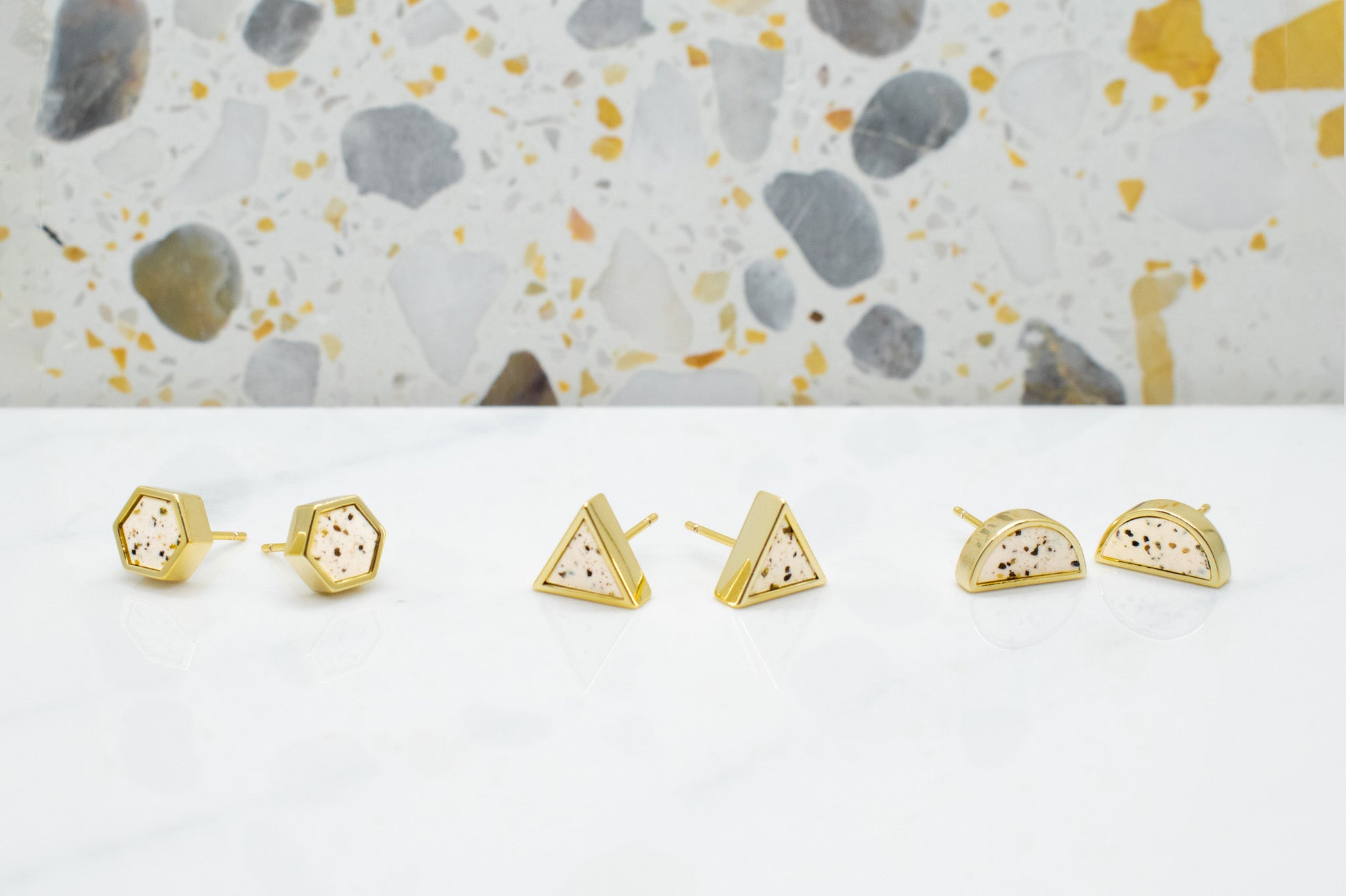 three pairs of dalmatian style terrazzo geometric gold stud earrings in hexagon, triangle, and half moons