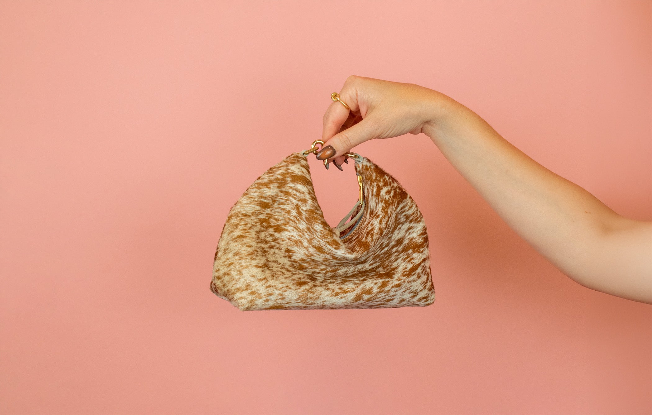 Hand holding a patterned handbag against a pink background
