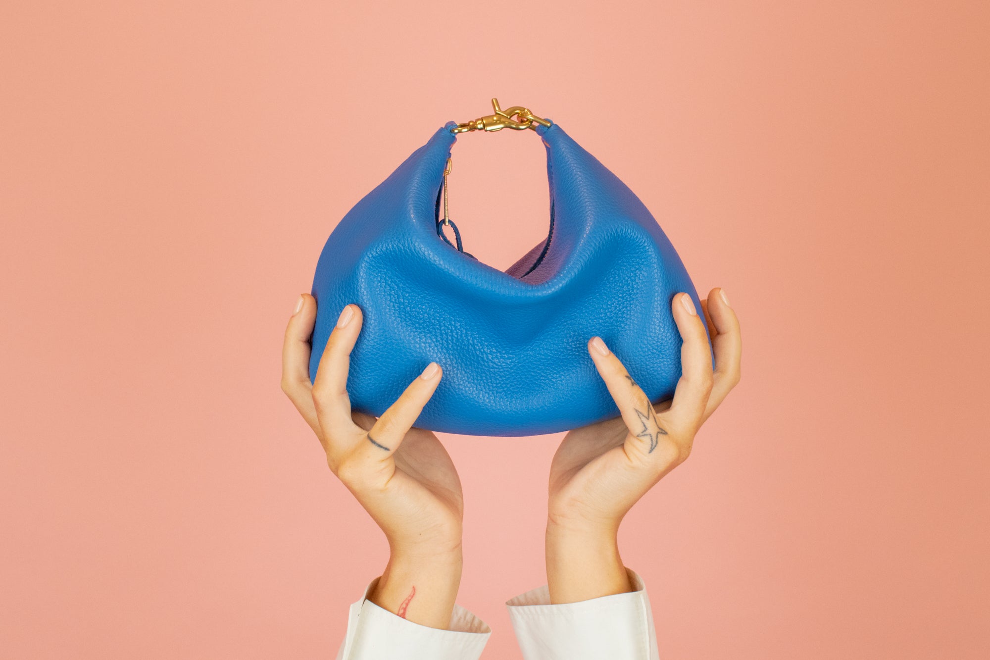 hands reaching towards the sky holding up primary blue leather mini crescent bag with relaxed silhouette and gold hardware