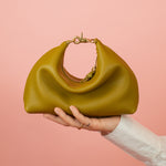 olive green leather mini crescent bag sitting a top an outstretched hand