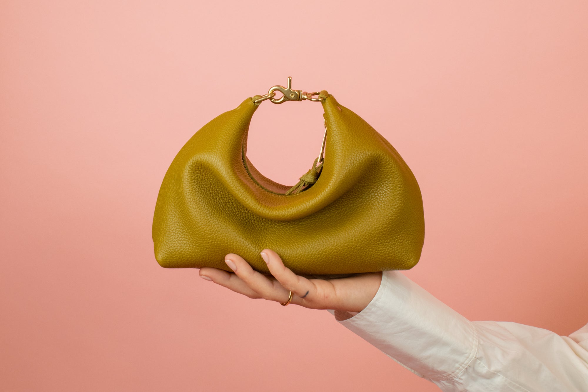 olive green leather mini crescent bag sitting a top an outstretched hand