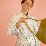 model in matching poka dot suit swings olive green leather shoulder bag with detachable strap towards camera