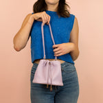 model holding up purple leather bucket bag with drawstring closure and gold hardware