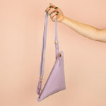 hand holding up leather crossbody slingbag displaying matching zipper fabric pull and strap 