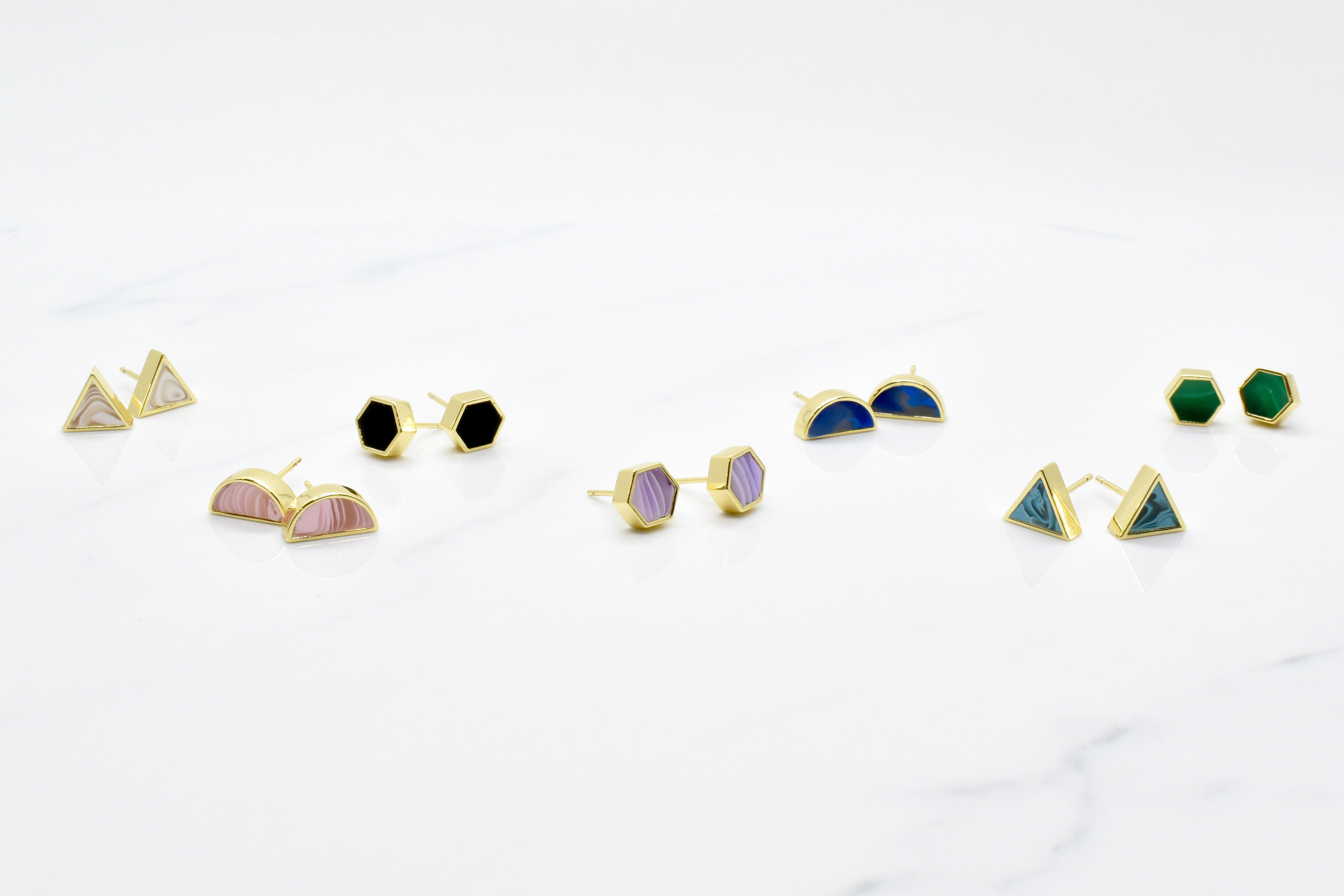 Pairs of new geo stud earrings in 14k gold, shown in triangle, half moon, and hexagon shapes
