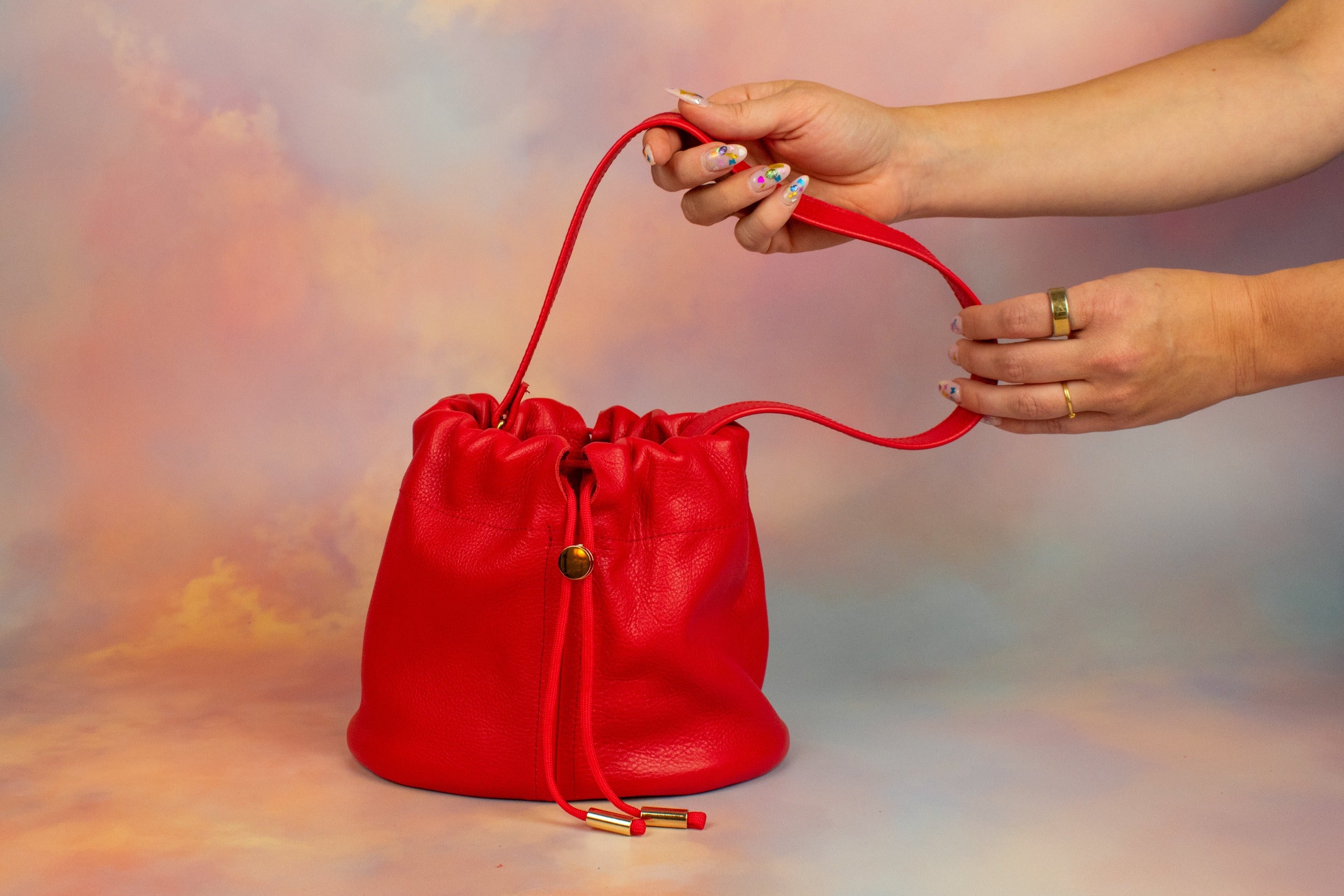 manicured hands displaying bright red luxury leather bucket bag drawstring closure gift for sister