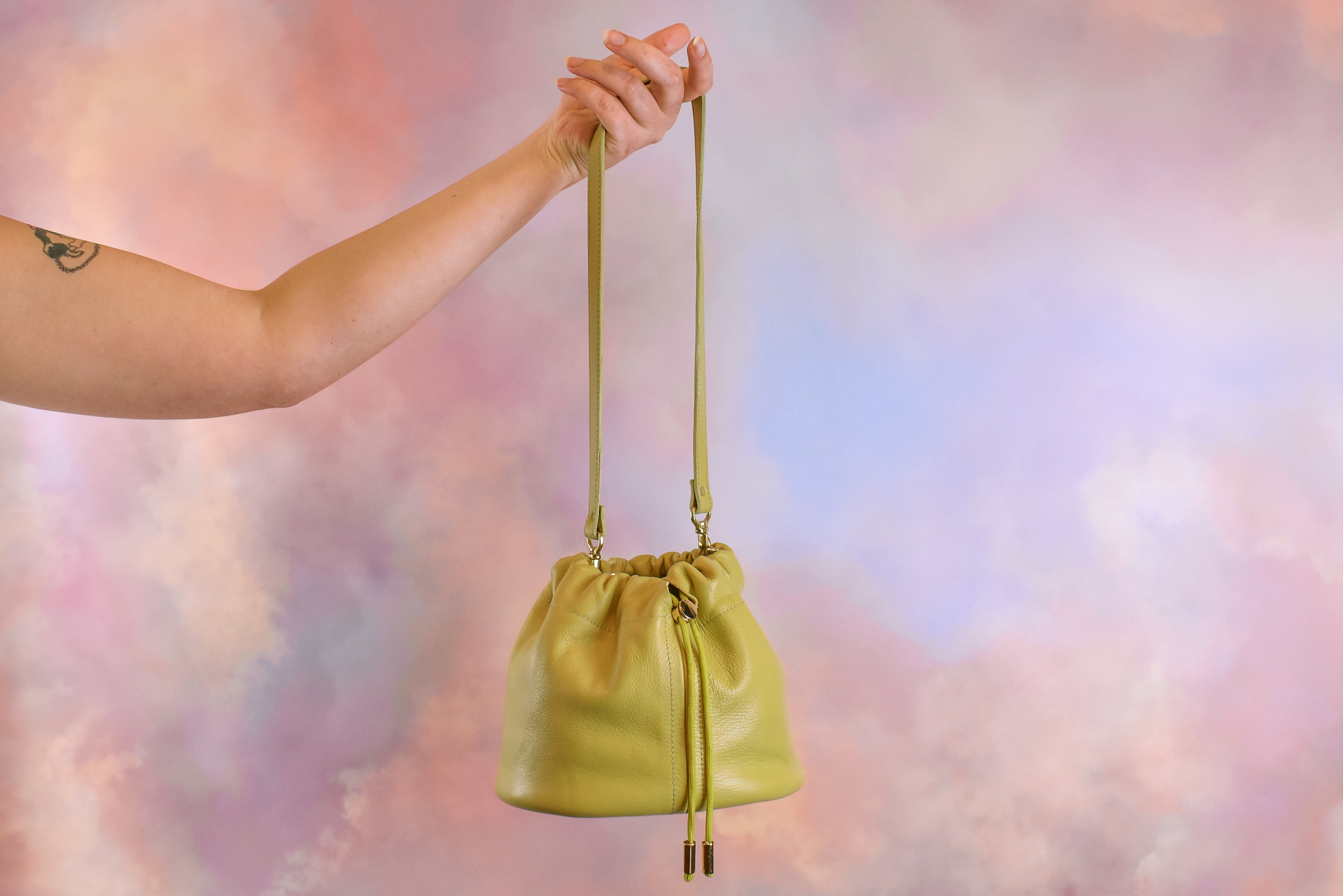 outstretched hand carrying spring green leather scrunch top drawstring bag 
