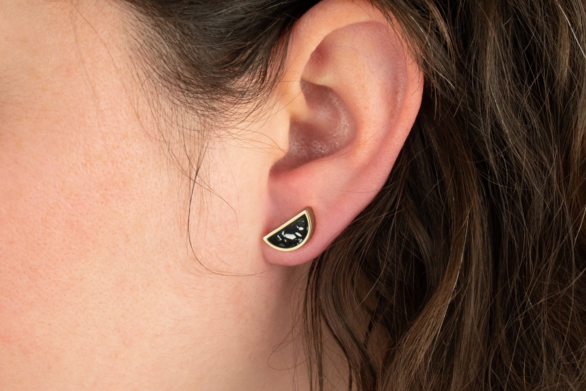 close up shot of model wearing semi circle geometric earrings handmade with matte black clay and tiny chips of white clay