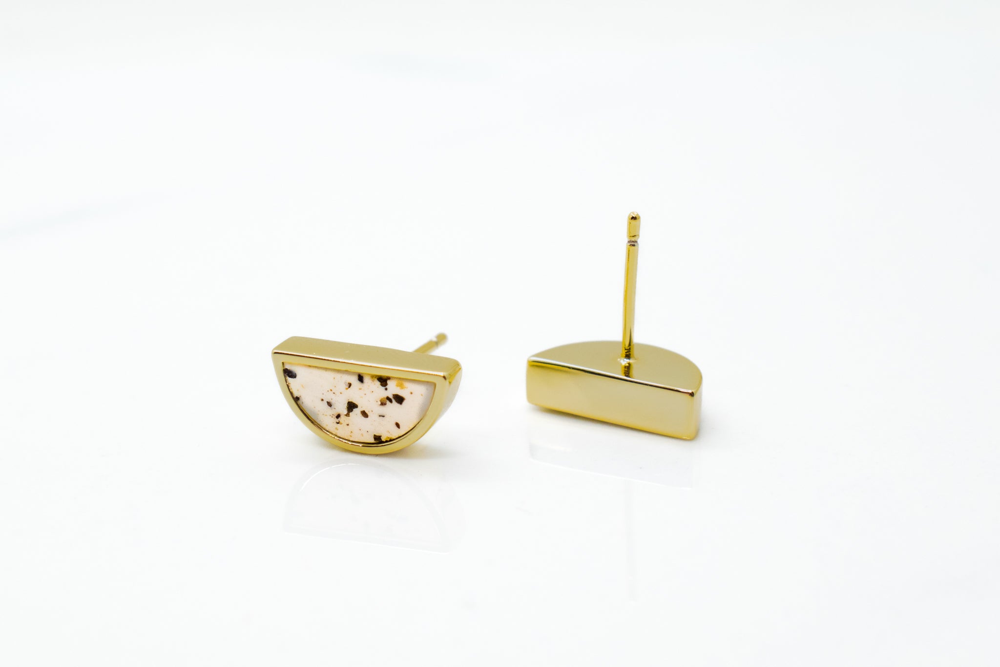 close up of gold and white minimalist geometric studs in terrazzo style on marble reflective background