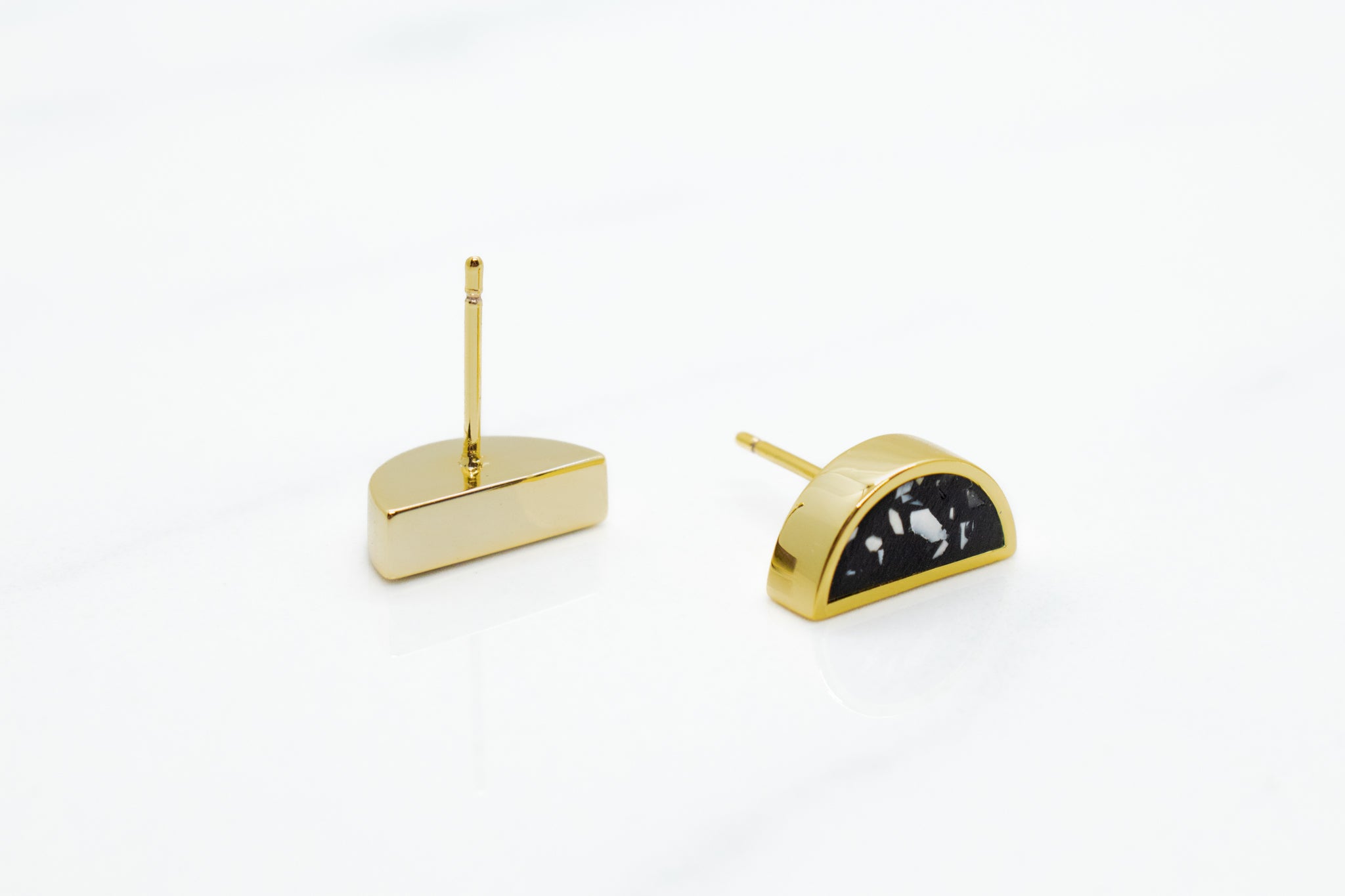 detail photo of 14k gold plated half moon earrings one laying faced down displaying gold plated post and the other front facing displaying black and white terrazo design