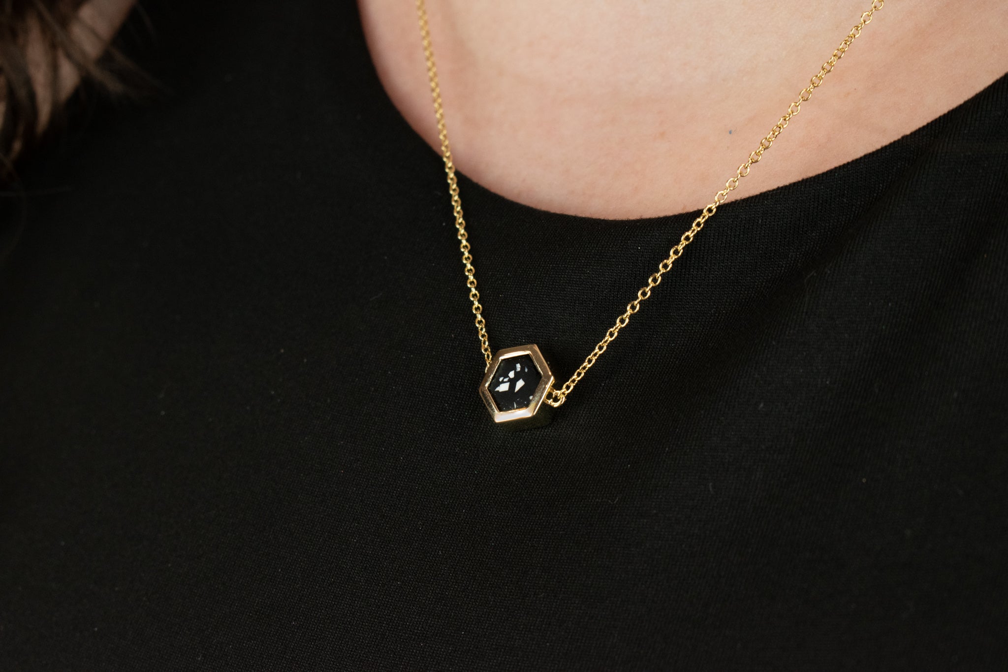 close up of 14k gold cable chain hexagon necklace with matte black clay featuring small chips of white clay in style of terrazzo