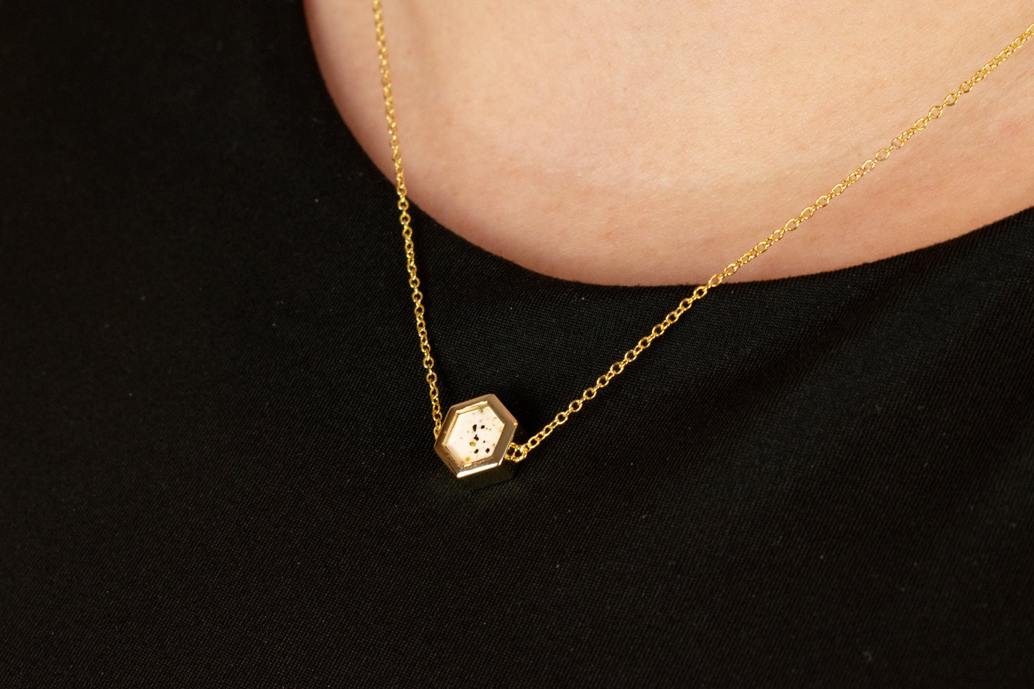 close up of gold cable chain choker in hexagon shape with white clay background speckled with flecks of black and brown